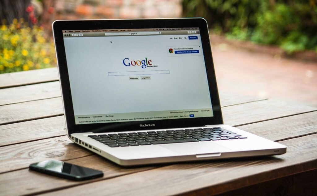 Why Every Business Needs A Website 2025 1 A MacBook Pro displaying Google Search on a wooden table outdoors, next to a smartphone.